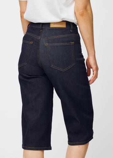 Dyp mørkeblå denim capris til dame i fargen Midnights sett bakfra i nærbilde for å vise passform og detaljer.