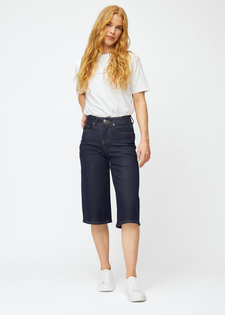 Helbilde av modell i dyp mørkeblå denim capris til dame i fargen Midnights med loose passform.