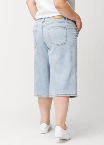 Løse, lyseblå Waves denimcapribukser sett bakfra på en plus-size-modell for å vise passform og lengde.