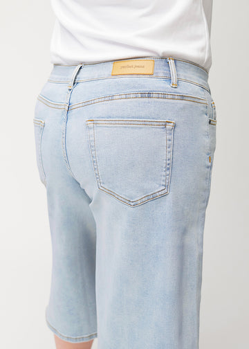 Nærbilde bakfra av løse, lyseblå Waves denimcapribukser på en plus-size-modell som viser passform og detaljer.