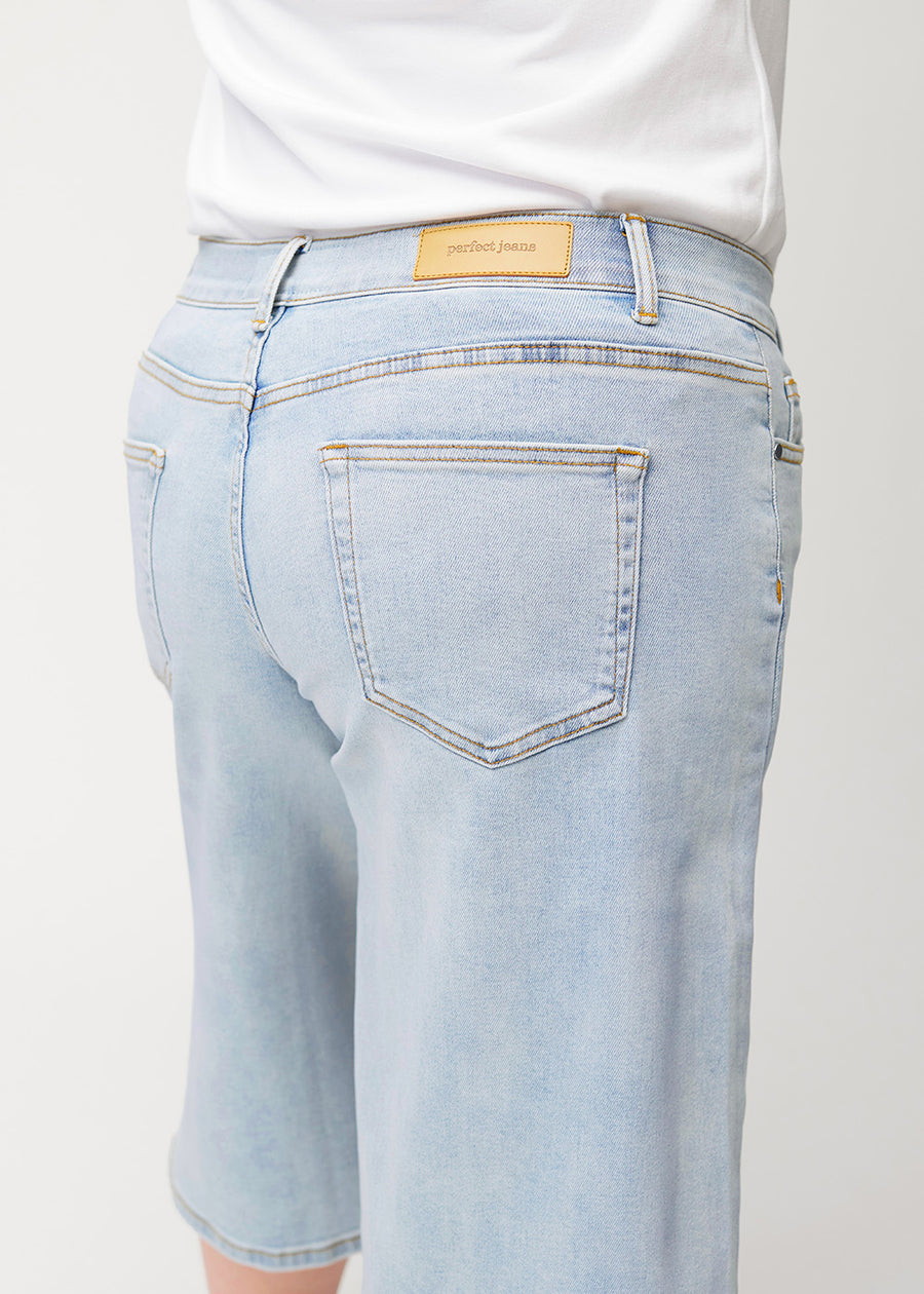 Nærbilde bakfra av løse, lyseblå Waves denimcapribukser på en plus-size-modell som viser passform og detaljer.