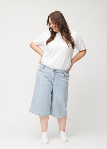 Helbilde av en plus-size-modell i løse, lyseblå Waves denimcapribukser som slutter rett under kneet.