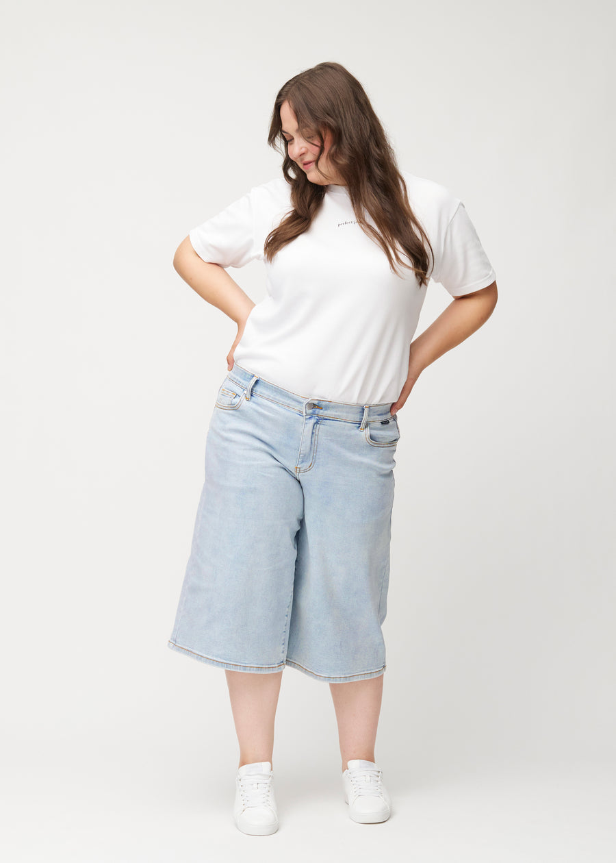 Helbilde av en plus-size-modell i løse, lyseblå Waves denimcapribukser som slutter rett under kneet.