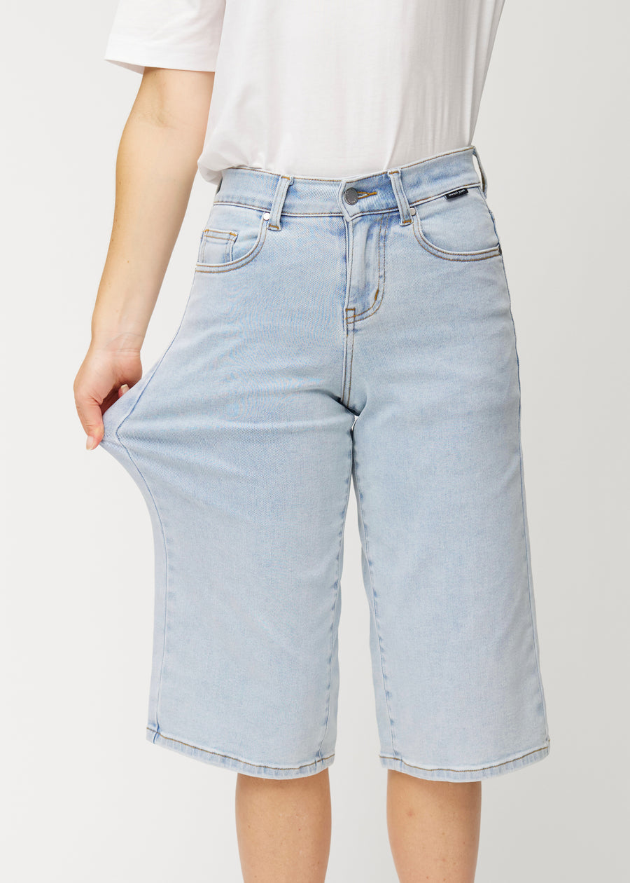 Modell strekker de løse, lyseblå Waves denimcapribuksene ved hoften for å vise materialets stretch.