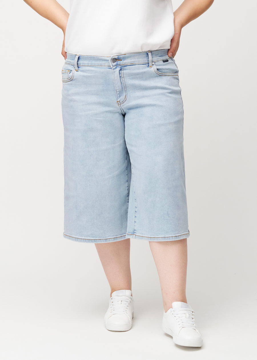 Plus-size-modell sett forfra i løse, lyseblå Waves denimcapribukser som sitter inntil hoftene og faller løst.
