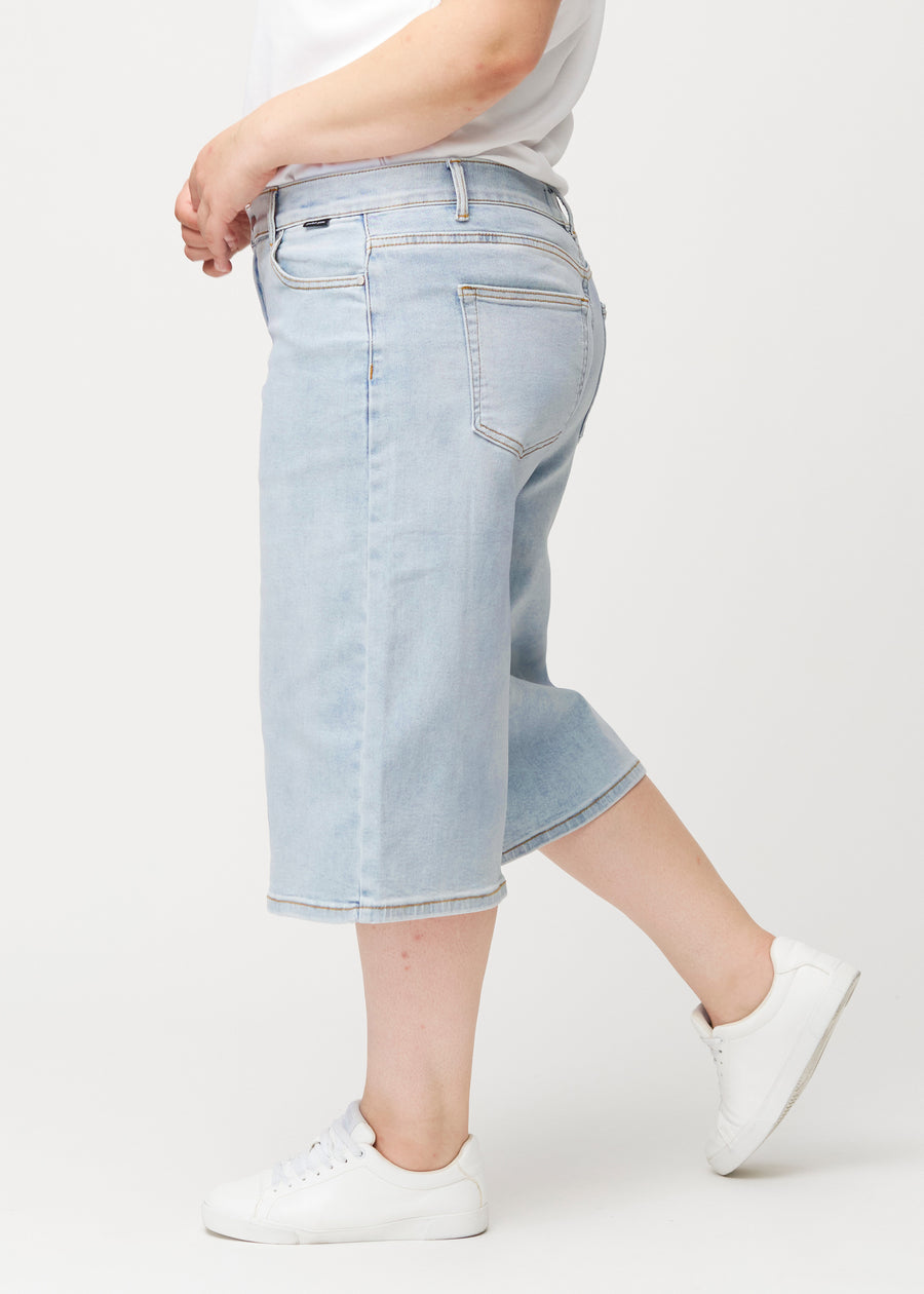 Løse, lyseblå Waves denimcapribukser sett fra siden på en plus-size-modell, som viser den romslige passformen og lengden til rett under kneet.