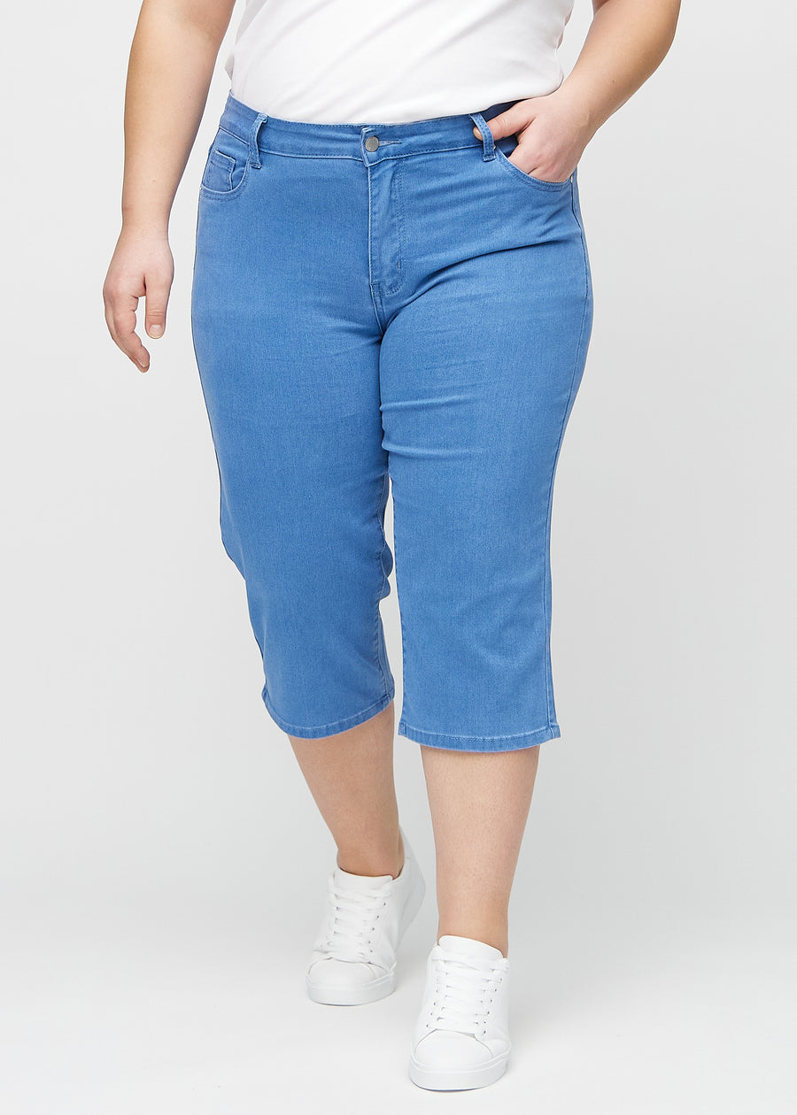 Blå regular capris, modellnavn Geraniums, som sitter tett langs benet og slutter rett under kneet på en plus-size-modell, sett forfra.