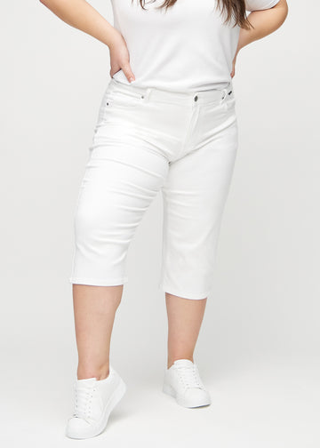 Hvite regular capris, modellnavn Marguerites, som sitter tett langs benet og slutter rett under kneet på en plus-size-modell, sett forfra.