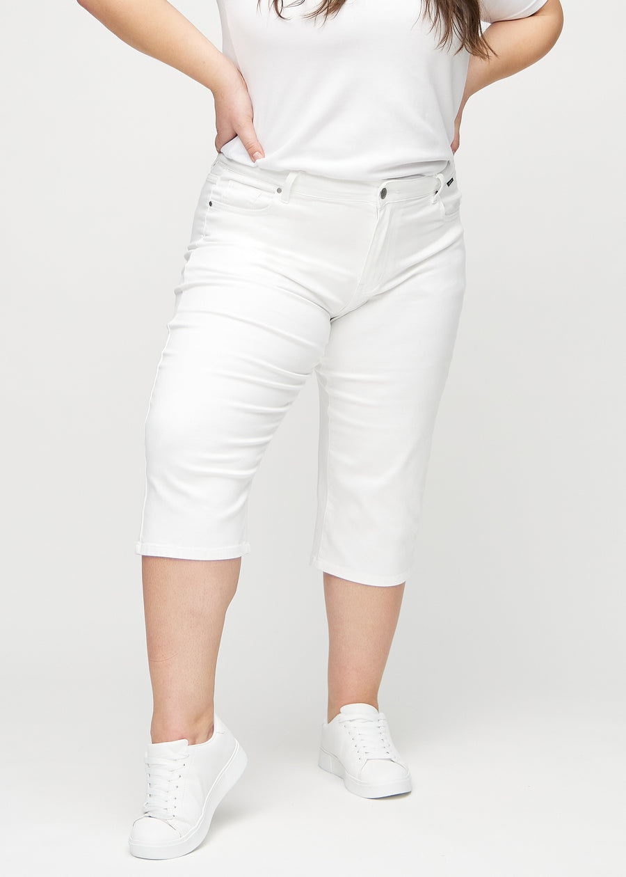 Hvite regular capris, modellnavn Marguerites, som sitter tett langs benet og slutter rett under kneet på en plus-size-modell, sett forfra.