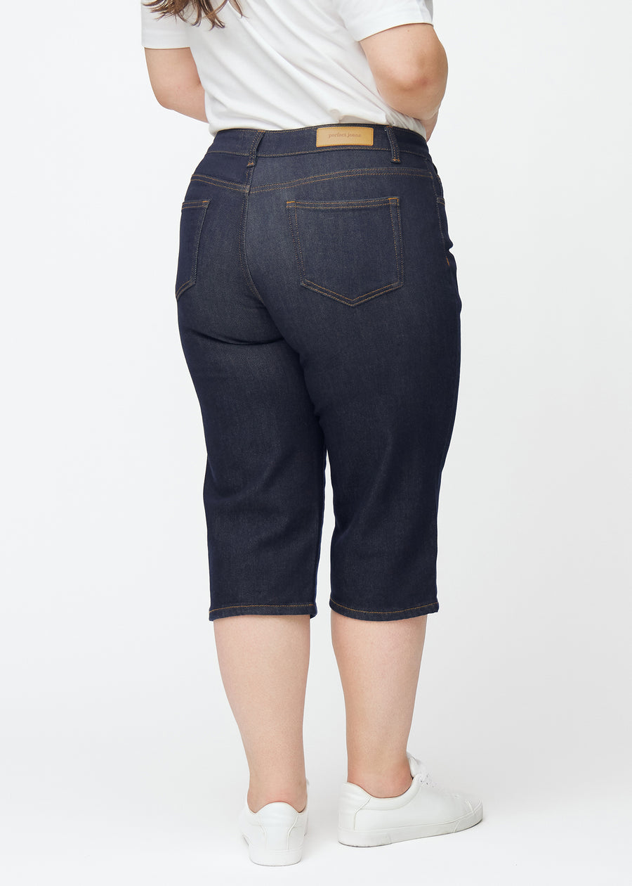 Dyp mørkeblå denim capris til dame i fargen Midnights sett bakfra på plus-size modell.