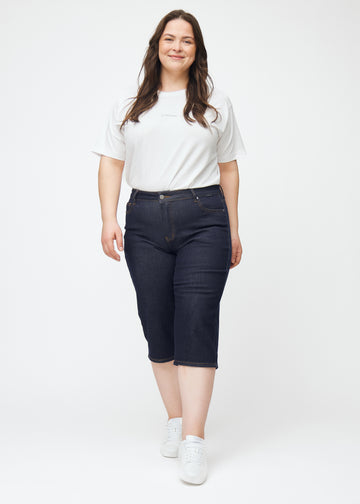 Helbilde av plus-size modell i dyp mørkeblå denim capris til dame i fargen Midnights med regular passform.