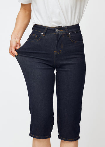 Modell strekker dyp mørkeblå denim capris til dame i fargen Midnights ved låret for å vise materialets stretch.