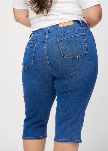 Mørk denim regular capris sett bakfra på nært hold på en plus-size modell for å vise detaljer.