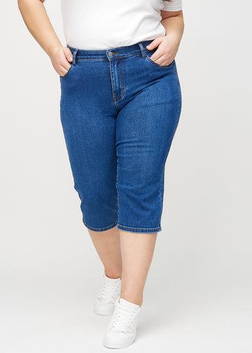 Mørk denim regular capris, modellnavn Oceans, som sitter rett langs benet og slutter rett under kneet på en plus-size modell, sett forfra.