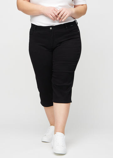 Svarte regular capris, modellnavn Ravens, som sitter tett langs benet og slutter rett under kneet på en plus-size modell, sett forfra.