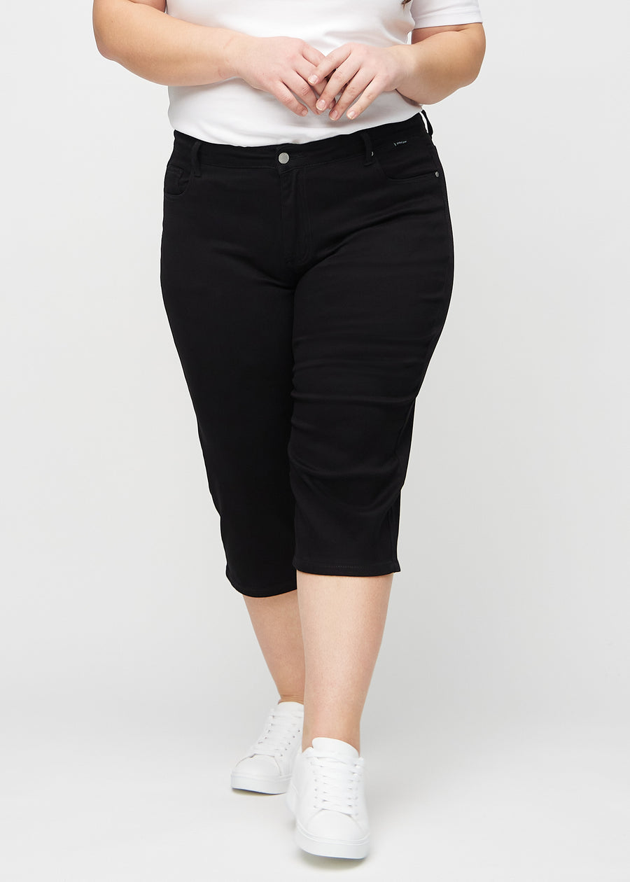 Svarte regular capris, modellnavn Ravens, som sitter tett langs benet og slutter rett under kneet på en plus-size modell, sett forfra.