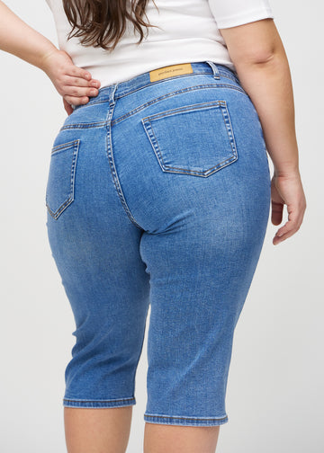 Denim regular capris sett bakfra på nært hold på en plus-size-modell for å vise detaljer.