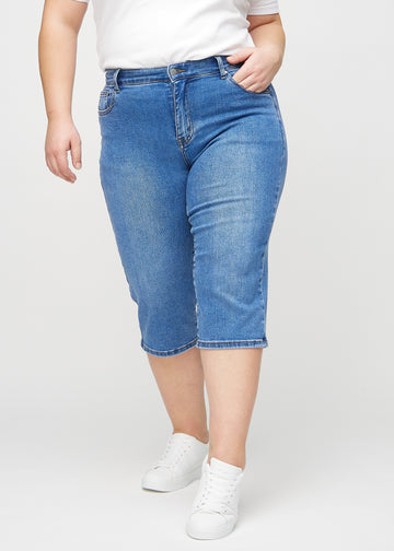 Denim regular capris, modellnavn Rivers, som sitter tett langs benet og slutter rett under kneet på en plus-size-modell, sett forfra.