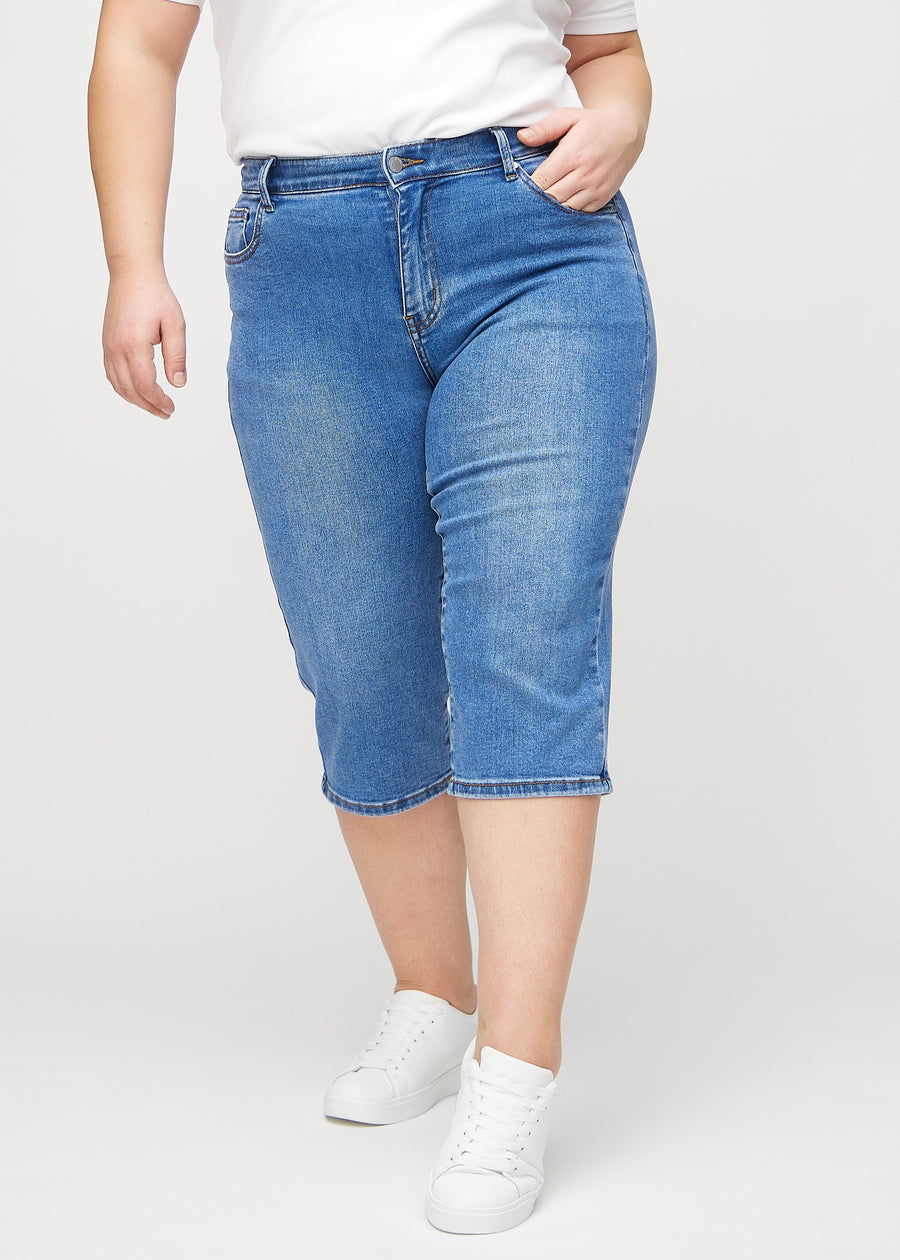 Denim regular capris, modellnavn Rivers, som sitter tett langs benet og slutter rett under kneet på en plus-size-modell, sett forfra.