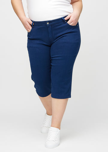 Mørkeblå regular capris, modellnavn Royals, som sitter tett langs benet og slutter rett under kneet på en plus-size-modell, sett forfra.