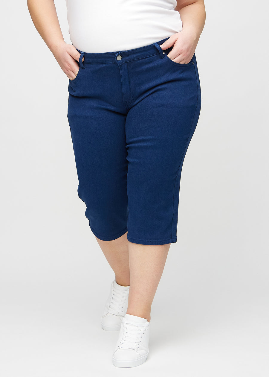 Mørkeblå regular capris, modellnavn Royals, som sitter tett langs benet og slutter rett under kneet på en plus-size-modell, sett forfra.