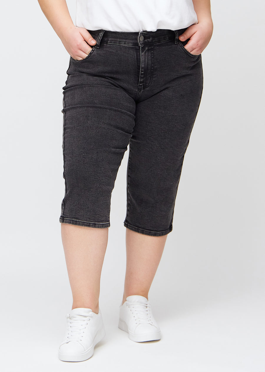 Mørkegrå denim regular capris, modellnavn Shadows, som sitter rett langs benet og slutter rett under kneet på en plus-size-modell, sett forfra.