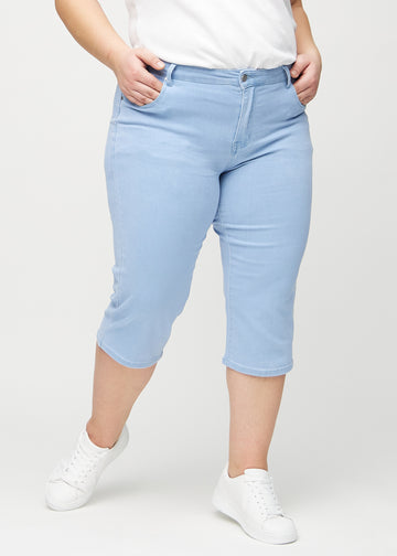Lyseblå regular capris, modellnavn Skies, som sitter rett langs benet og slutter rett under kneet på en plus-size-modell, sett forfra.