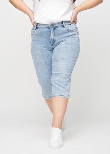 Lys denim regular capris, modellnavn Waves, som sitter rett langs benet og slutter rett under kneet på en plus-size-modell, sett forfra.