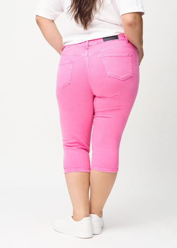 Skinny-capris til kvinner i pastellrosa jeansstoff, fargen Flamingos. Sett bakfra på en plus size-modell, med fokus på passform og baklommer.