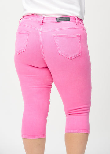 Skinny-capris til kvinner i pastellrosa jeansstoff, fargen Flamingos. Nærbilde bakfra på en plus size-modell, med fokus på lommer og sømmer.
