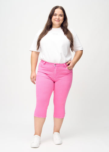 Skinny-capris til kvinner i pastellrosa jeansstoff, fargen Flamingos. Helhetsbilde av en plus size-modell med capris på.