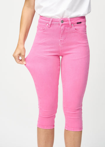 Skinny-capris til kvinner i pastellrosa jeansstoff, fargen Flamingos. En modell strekker stoffet for å vise fleksibiliteten.