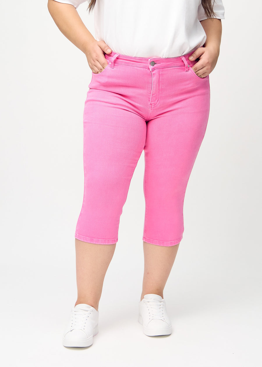 Skinny-capris til kvinner i pastellrosa jeansstoff, fargen Flamingos. Sett forfra på en plus size-modell, med tettsittende ben til rett under kneet.