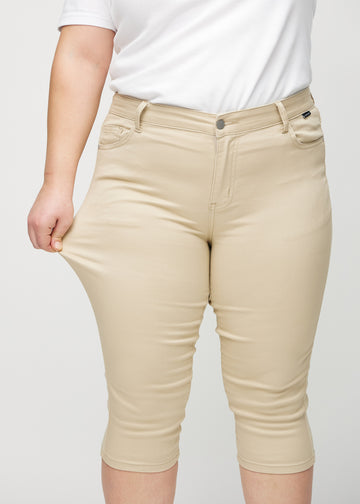 Skinny-capris til kvinner i beige jeansstoff, fargen Gazelles. En plus size-modell strekker stoffet for å vise fleksibiliteten.