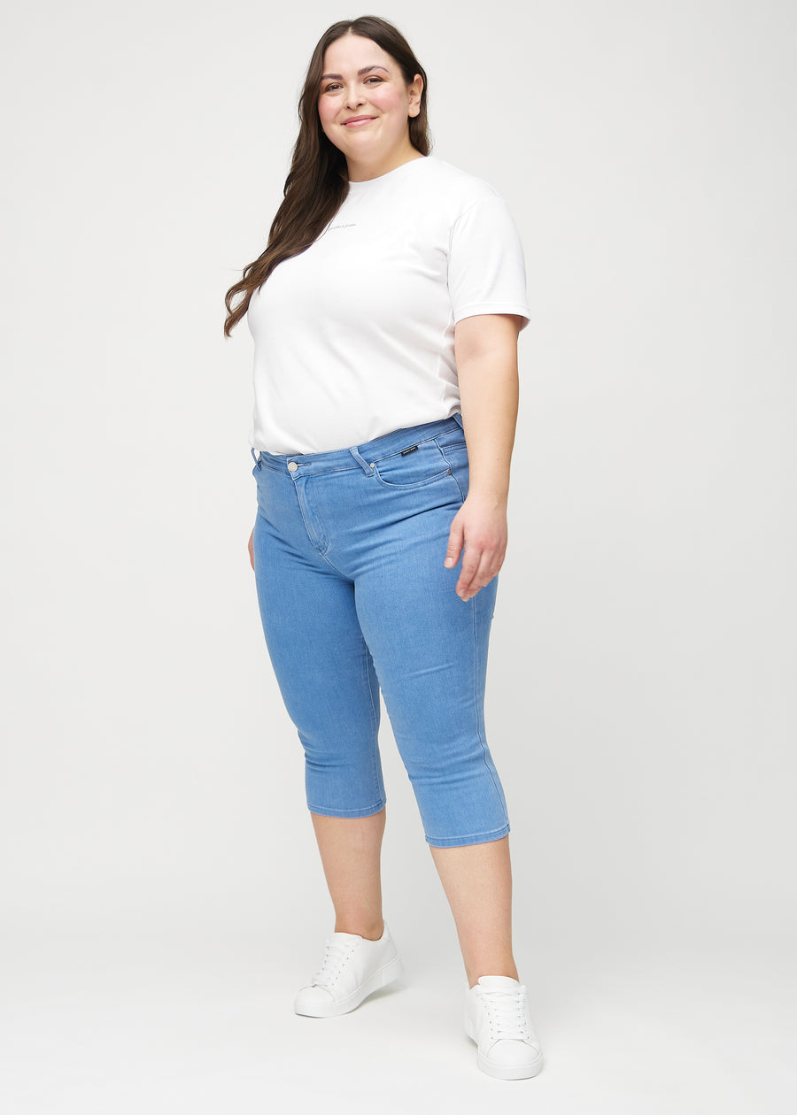Skinny-capris til kvinner i blått jeansstoff, fargen Geraniums. Helhetsbilde av en plus size-modell med capris på.