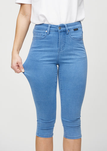 Skinny-capris til kvinner i blått jeansstoff, fargen Geraniums. En modell strekker stoffet for å vise fleksibiliteten.