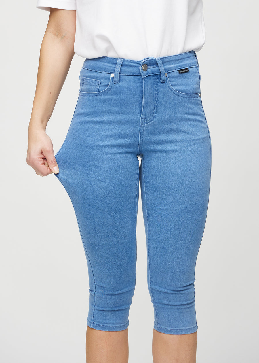 Skinny-capris til kvinner i blått jeansstoff, fargen Geraniums. En modell strekker stoffet for å vise fleksibiliteten.