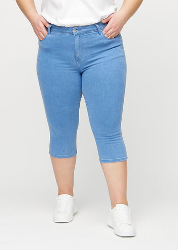 Skinny-capris til kvinner i blått jeansstoff, fargen Geraniums. Sett forfra på en plus size-modell, med tettsittende ben til rett under kneet.