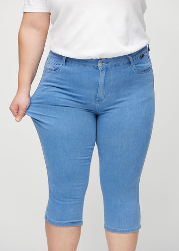Skinny-capris til kvinner i blått jeansstoff, fargen Geraniums. En plus size-modell strekker stoffet for å vise fleksibiliteten.