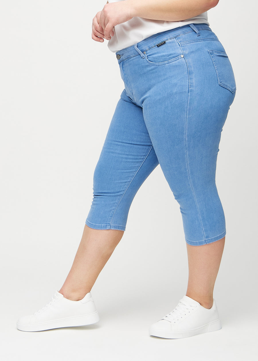 Skinny-capris til kvinner i blått jeansstoff, fargen Geraniums. Sett fra siden på en plus size-modell, med tettsittende passform.