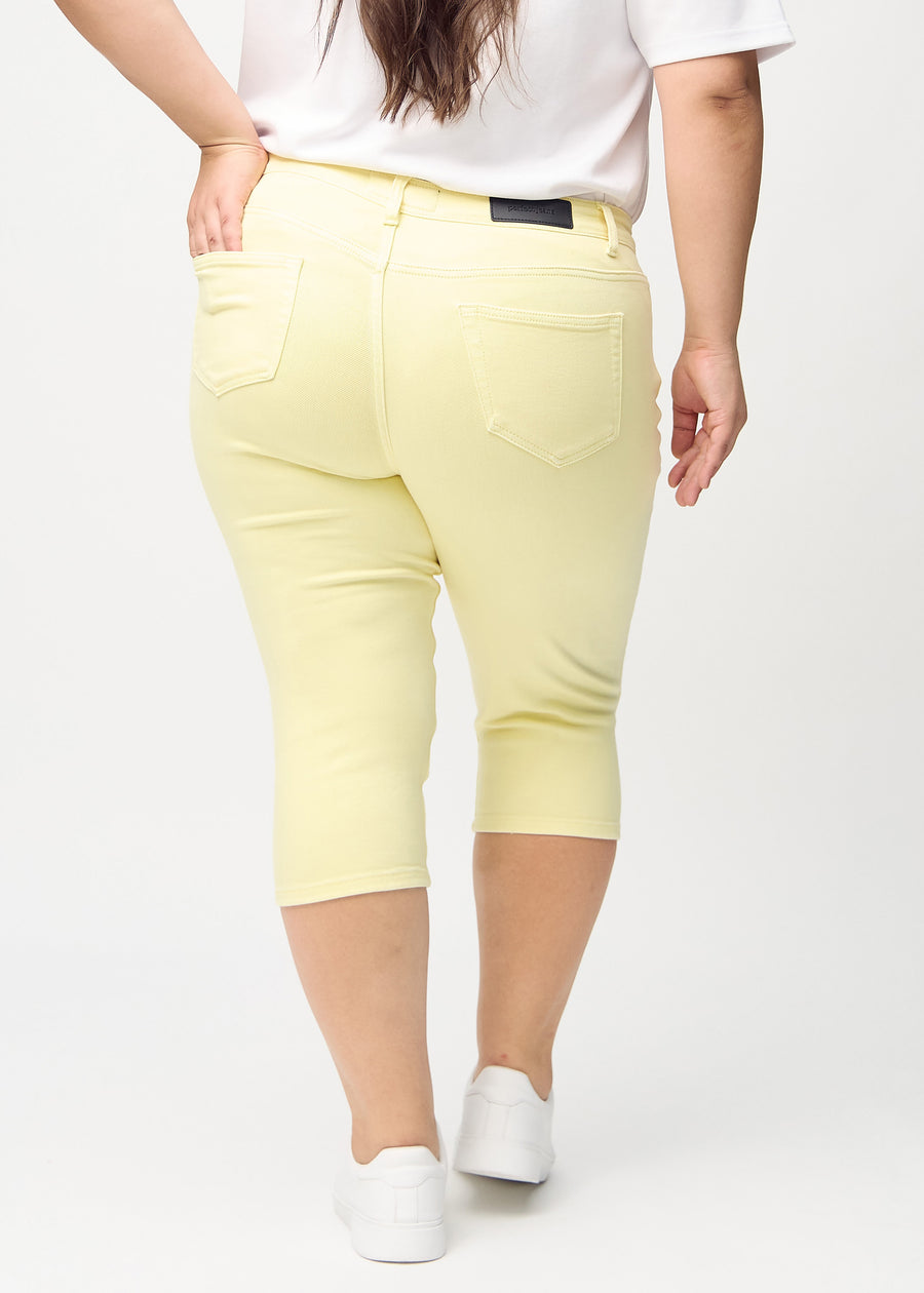 Skinny-capris til kvinner i pastellgult jeansstoff, fargen Lemonades. Sett bakfra på en plus size-modell, med fokus på passform og baklommer.