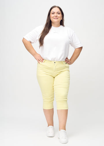 Skinny-capris til kvinner i pastellgult jeansstoff, fargen Lemonades. Helhetsbilde av en plus size-modell med capris på.