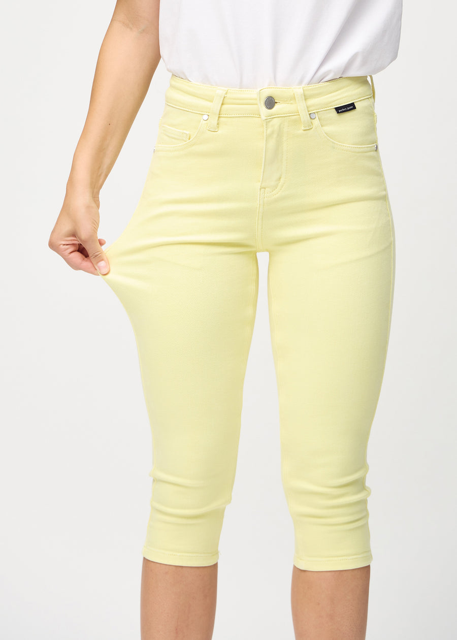 Skinny-capris til kvinner i pastellgult jeansstoff, fargen Lemonades. En modell strekker stoffet for å vise fleksibiliteten.