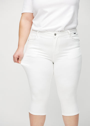 Skinny-capris til kvinner i hvitt jeansstoff, fargen Marguerites. En plus size-modell strekker stoffet for å vise fleksibiliteten.