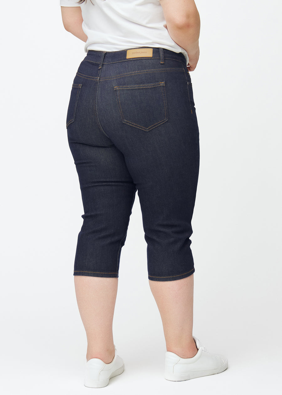 Dyp mørkeblå denim capris til dame i fargen Midnights sett bakfra, slik at lengden under kneet vises.