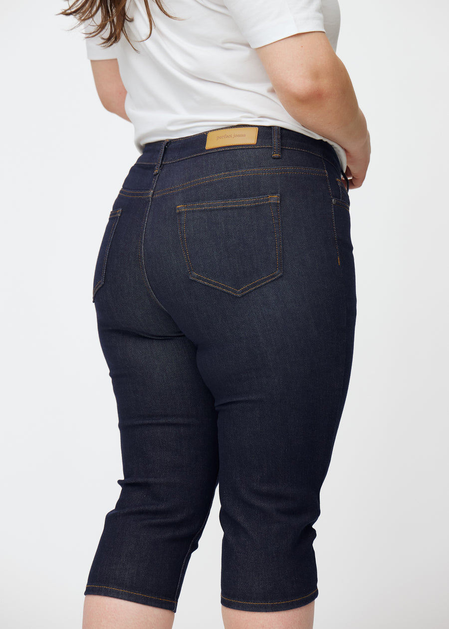 Dyp mørkeblå denim capris til dame i fargen Midnights sett bakfra i nærbilde på plus-size modell.
