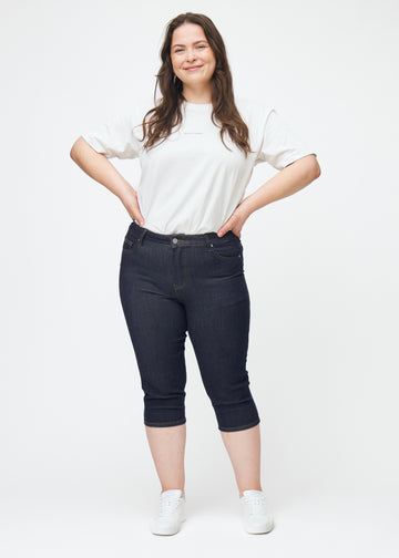 Helbilde av plus-size modell i dyp mørkeblå denim capris til dame i fargen Midnights med skinny passform.