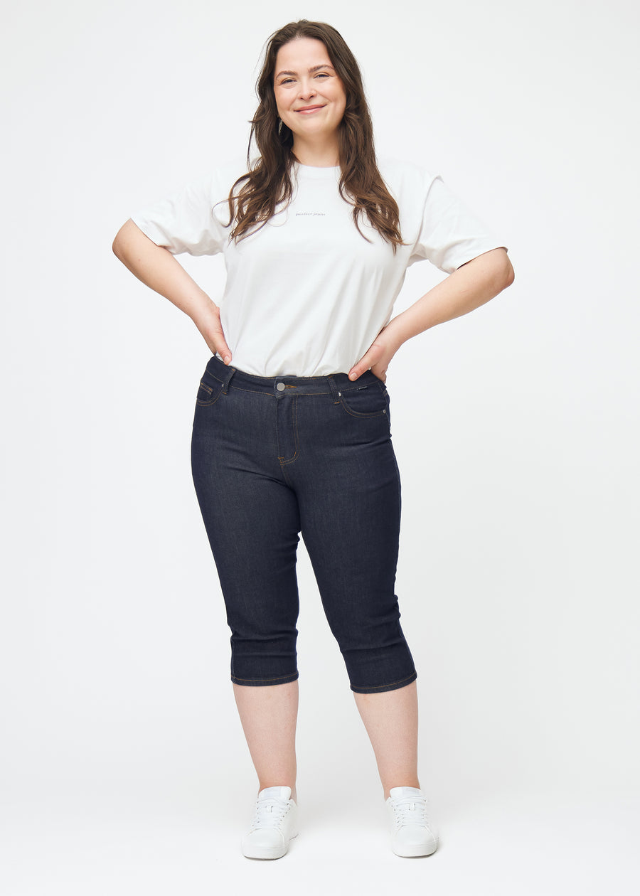 Helbilde av plus-size modell i dyp mørkeblå denim capris til dame i fargen Midnights med skinny passform.