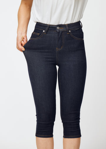 Modell strekker dyp mørkeblå denim capris til dame i fargen Midnights ved låret for å vise materialets stretch.