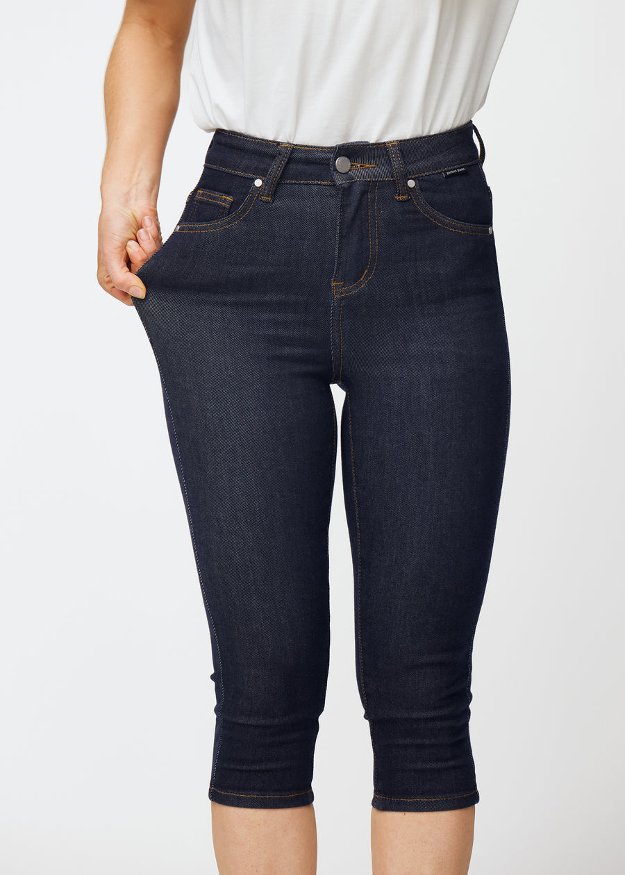 Modell strekker dyp mørkeblå denim capris til dame i fargen Midnights ved låret for å vise materialets stretch.